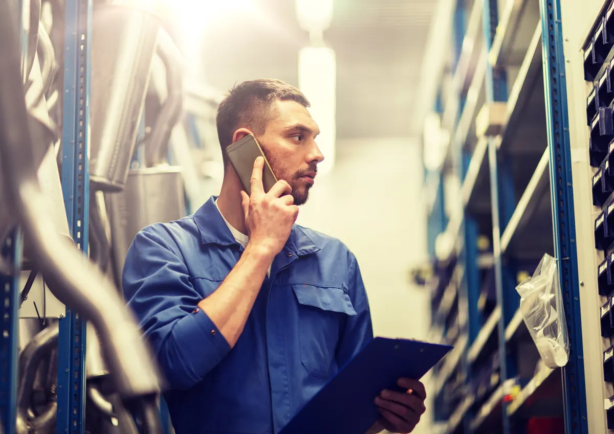 Mechanic taking a phone call with a clipboard in the shop